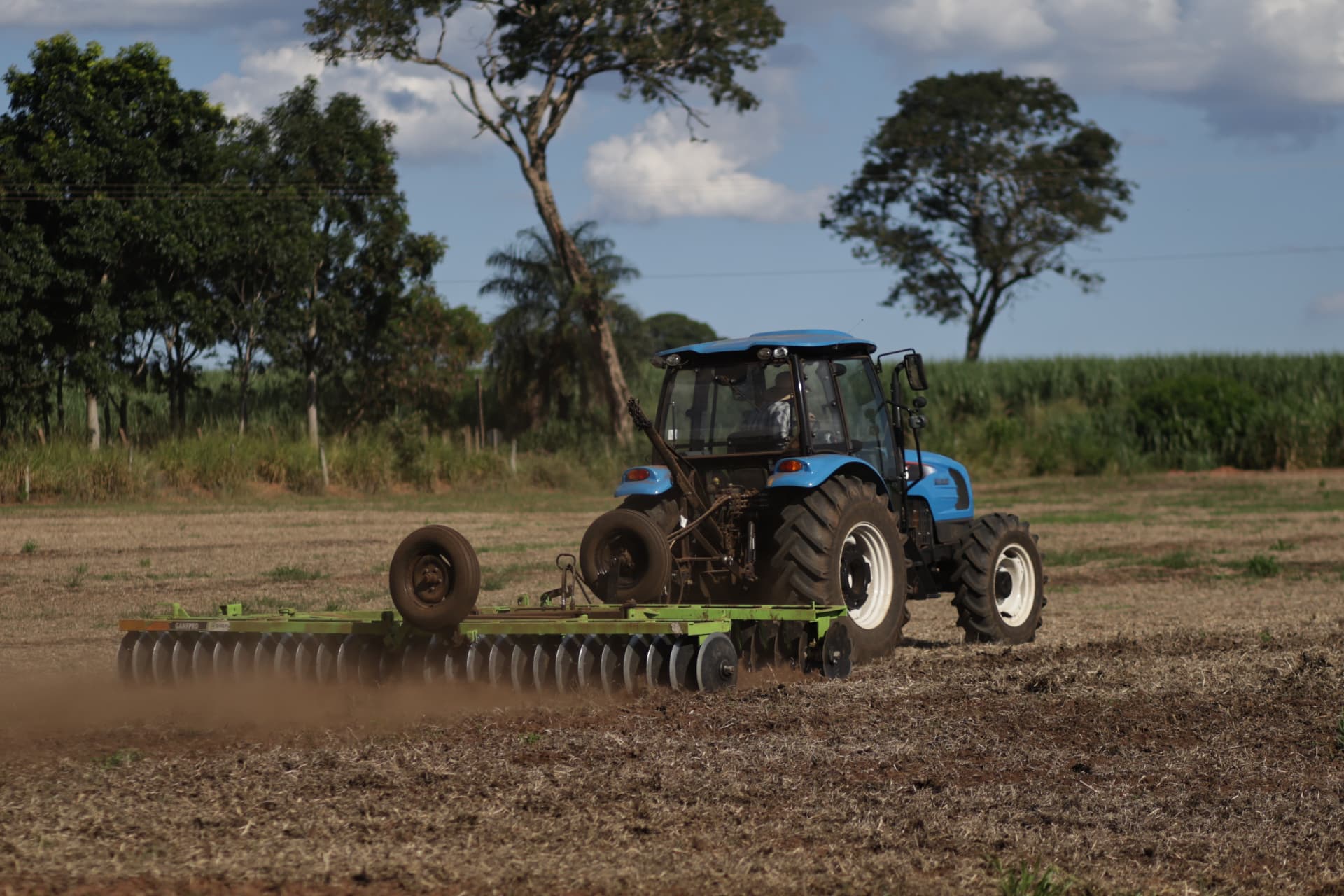 Trator azul realizando gradagem em área de plantio