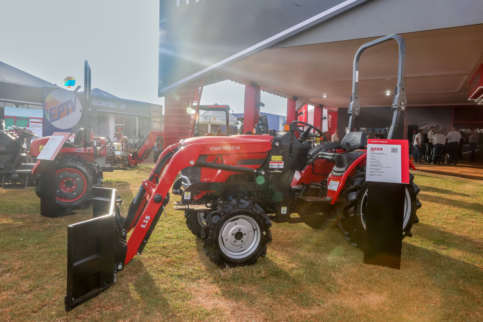 Trator Mahindra com implemento frontal exposto em estande de feira do agro